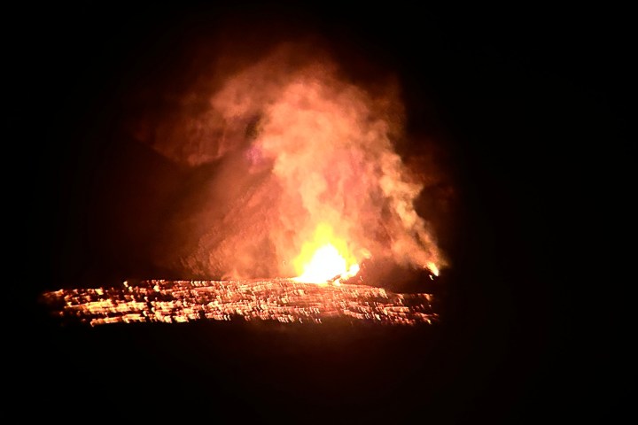 Night scene of lava flow and bright volcanic eruption with rising smoke.