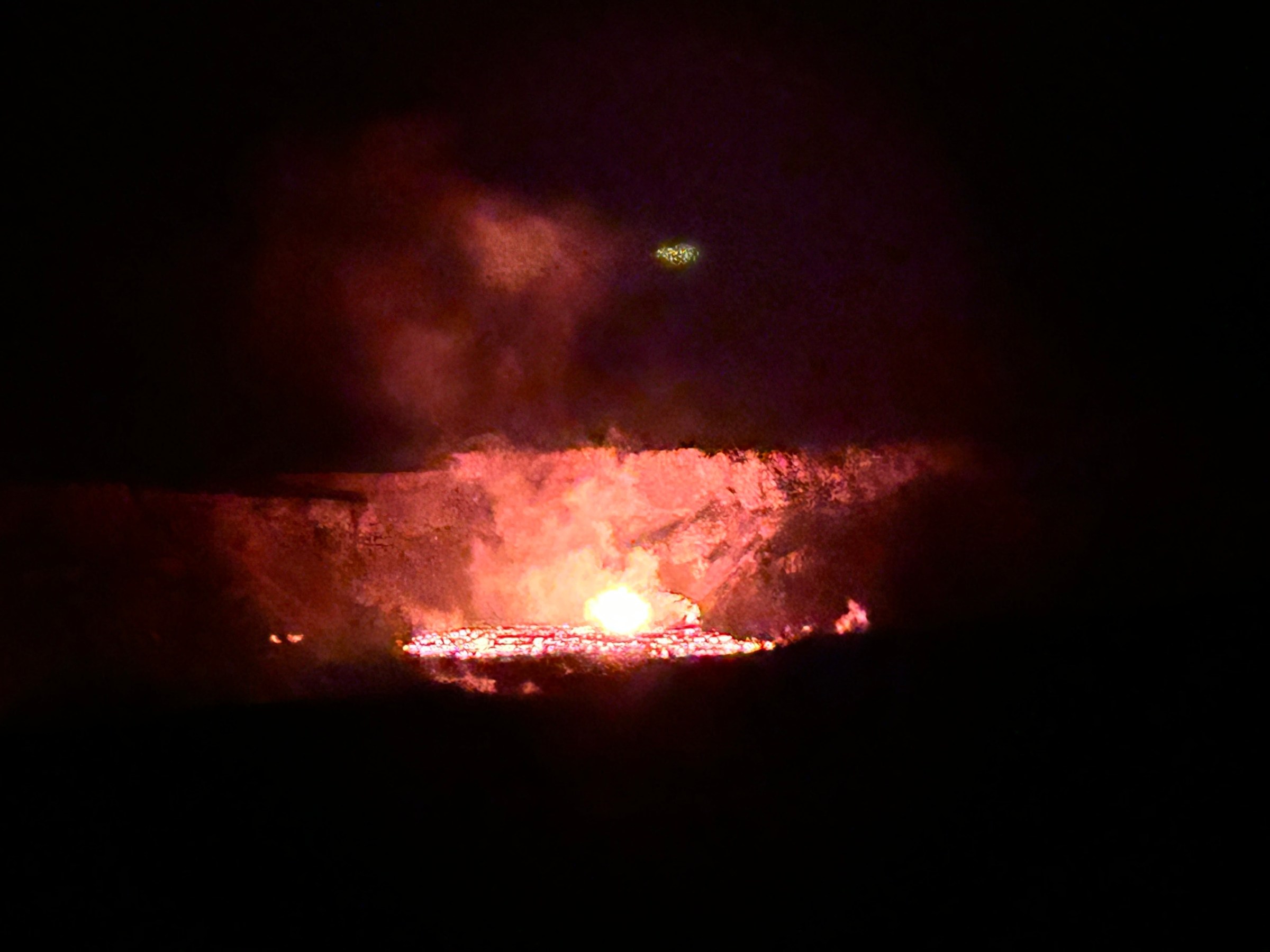 Glowing lava inside a crater at night with smoke rising.
