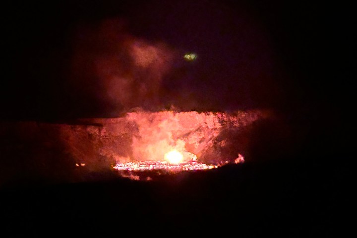 Glowing lava inside a crater at night with smoke rising.